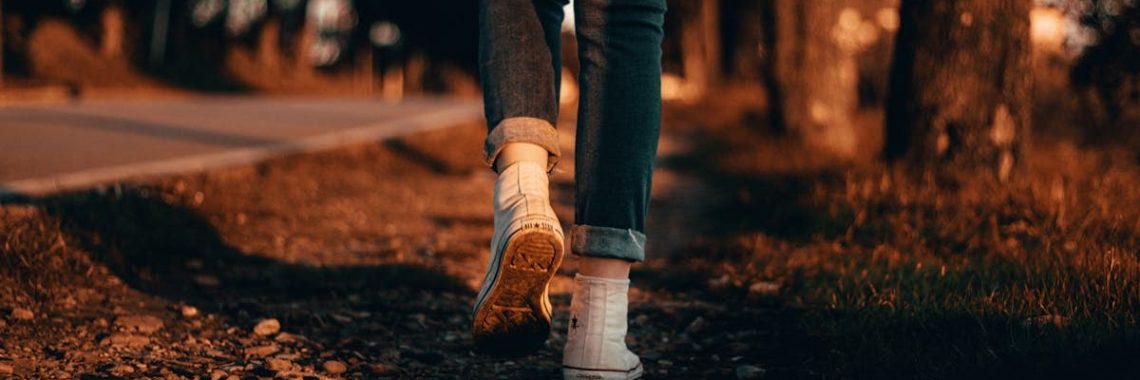 A person in jeans and sneakers walks along a forest path at sunset in Italy.