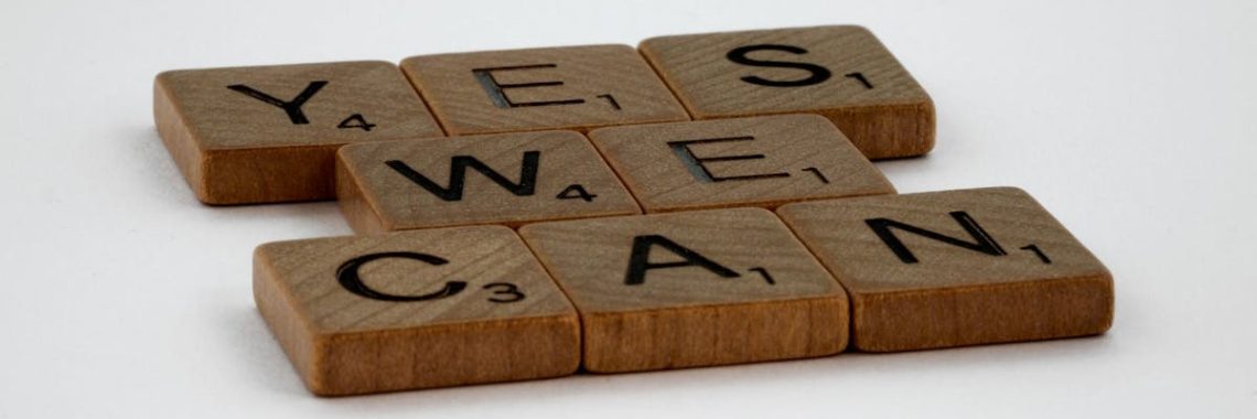 Scrabble tiles spelling 'Yes We Can' on a white background, conveying encouragement.